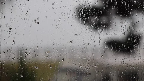 Raindrops trickling down a window pane, against a blurred background with trees Stock Footage 132064378