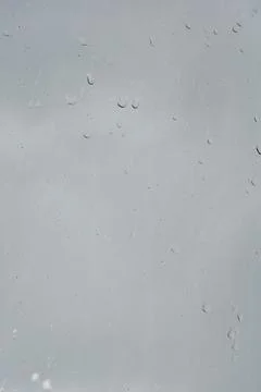 Raindrops trickling down a window pane against a grey overcast sky Stock Photos