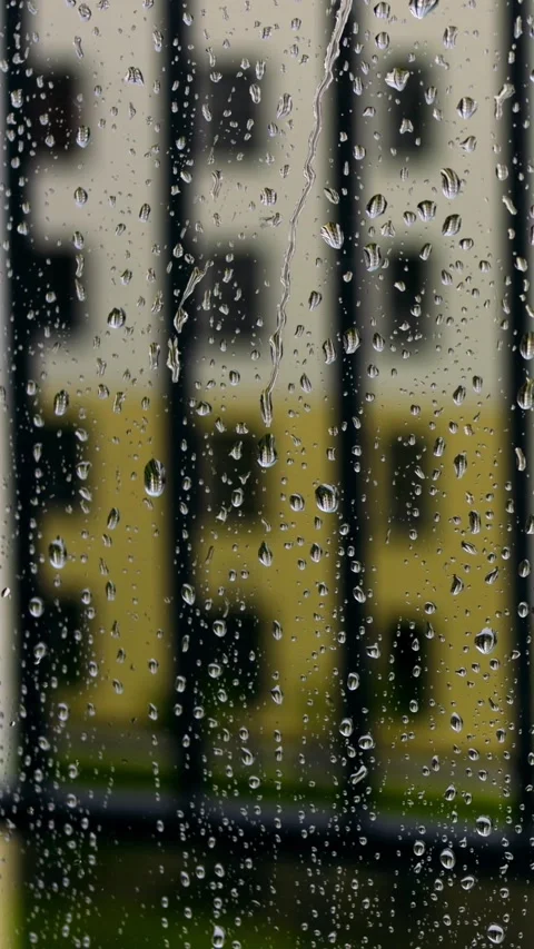 Raindrops on window with blurred building, black railing silhouettes and yellow Stock Footage 344741156