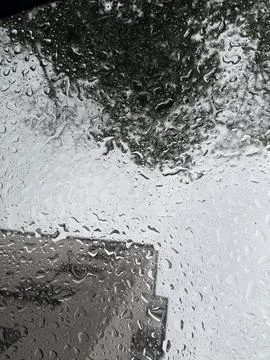 Raindrops on a window with a blurred view of a building and trees Stock Photos