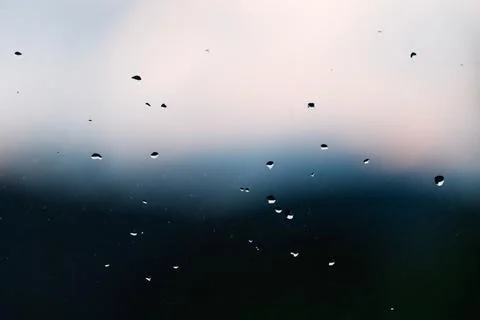 Raindrops on the window with clouds over the mountains unfocused in the backg Stock Photos