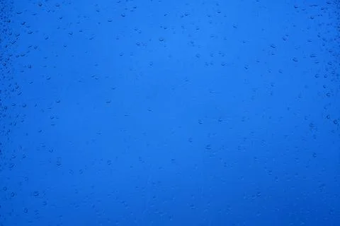 Raindrops on a window glass on a blurred blue background Stock Photos