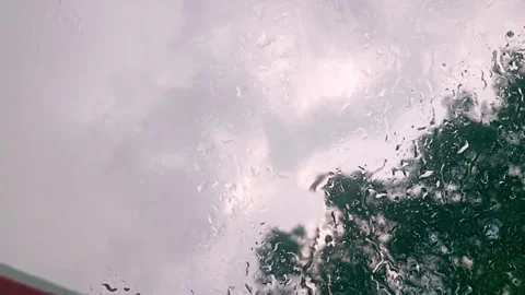 Raindrops on Window Glass with Blurred Trees Background and Cloudy Sky on Ra Stock Footage 331718237