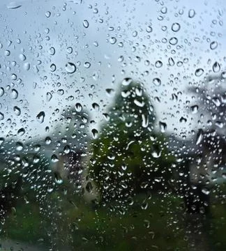 Raindrops on Window Glass with Blurred Trees and Stormy Sky Background Stock Photos