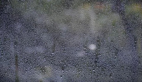 Raindrops on window glass surface with trees and nature blurred background Stock Photos