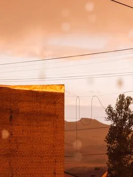 Raindrops on window overlooking industrial landscape in warm orange sunset light Stock Photos