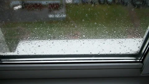 Raindrops on window pane with blurred background of green grass and buildings Stock Footage 323909745