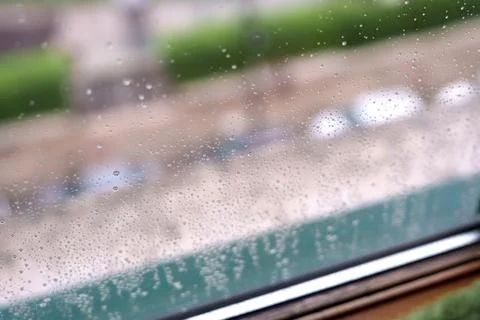 Raindrops on a window pane with blurred parked cars Stock Photos