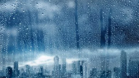 Raindrops on a window pane overlooking a blurred city skyline during a mood.. 스톡 사진