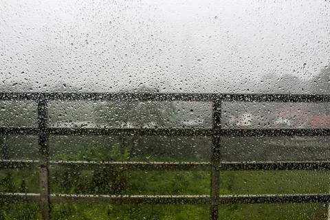 Raindrops on window pane with white mist on balcony railing background Stock Photos