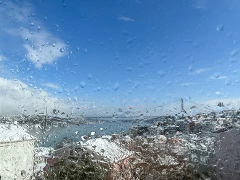 Raindrops on windowpane over blurred sky and city view under snow Stock Photos