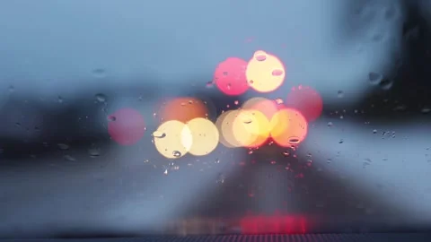 Raindrops on windshield with blurred car lights in motion. Rainy traffic bokeh b Stock Footage 329623864