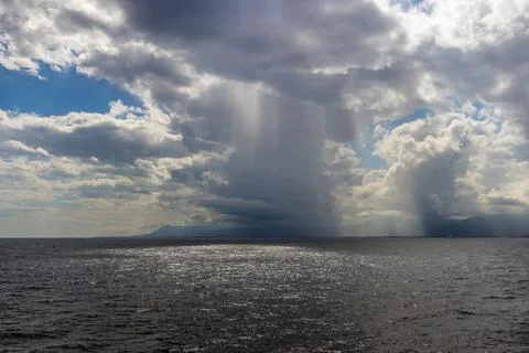 Rainfall over the sea with dramatic clouds, sunlight reflections, and dista.. 写真素材