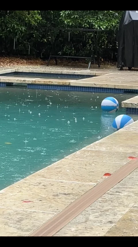 Rainfall on poolside with floating beach balls under overcast skies Stock Footage 315524684