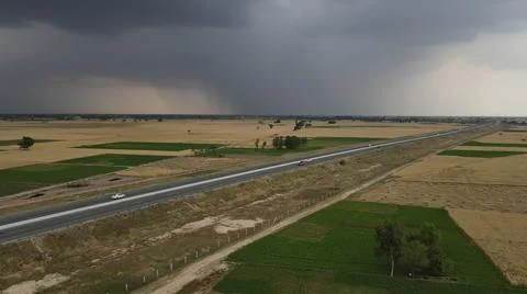 Raining clouds around the wheat crop adjacent to Motorway with a car Stock Photos