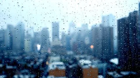 Raining day scene of rain drops on window with blurred city skyline background Stock Photos