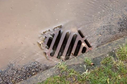 Rainwater flowing down road drain, UK Stock Photos