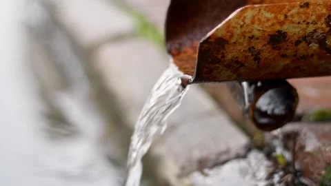 Rainwater flows from rusty metal gutter into stone drain, capturing urban Stock Footage 309677400