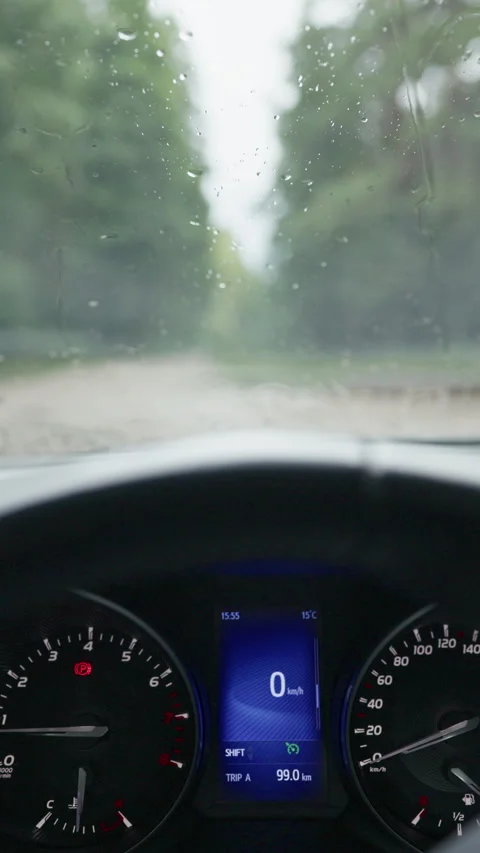 Rainy car interior view with dashboard gauges, wet windshield, blurred road Stock Footage 344772816