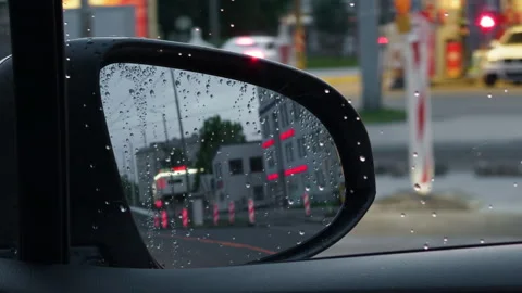 Rainy car side mirror with water droplets reflecting blurred street, traffic Stock Footage 344995914