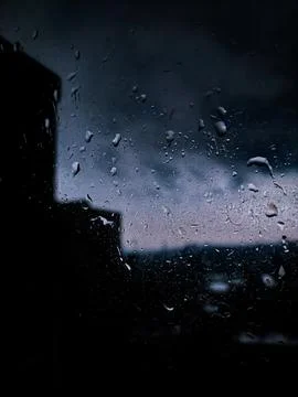 A rainy day, raindrops on window cloudy sky and blurry city buildings background Stock Photos