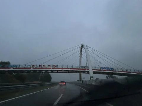 Rainy highway beneath cable stayed bridge with wet reflective road, distant car Stock Photos