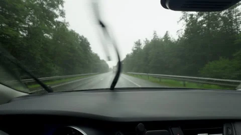 Rainy highway drive seen through car windshield with wipers sweeping past forest Stock Footage 345764922
