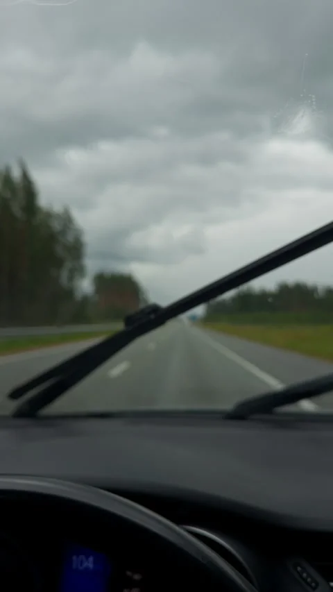 Rainy highway view through car windshield with moving wiper and cloudy sky over Stock Footage 345452755