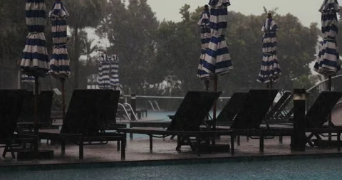 Rainy poolside scene with empty lounge chairs and umbrellas, overcast Stock Footage 312000831