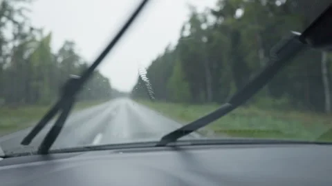 Rainy road seen through car windshield with moving wipers and blurred forest Stock Footage 344771269