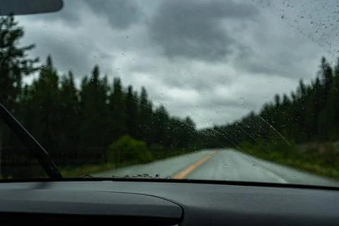 Rainy road trip through forest. View through the windshield of the car. Stock Photos