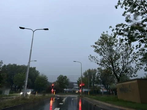 Rainy urban road intersection with red traffic lights, wet reflective pavement Stock Photos