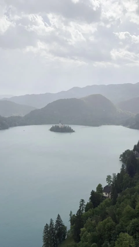 Rainy view of Lake Bled with island church and sun rays through clouds. The vide Stock Footage 337534456