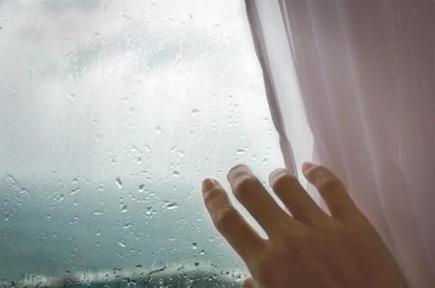 Rainy weather - a woman's hand pulls the blind from the rainy window. Stock Photos