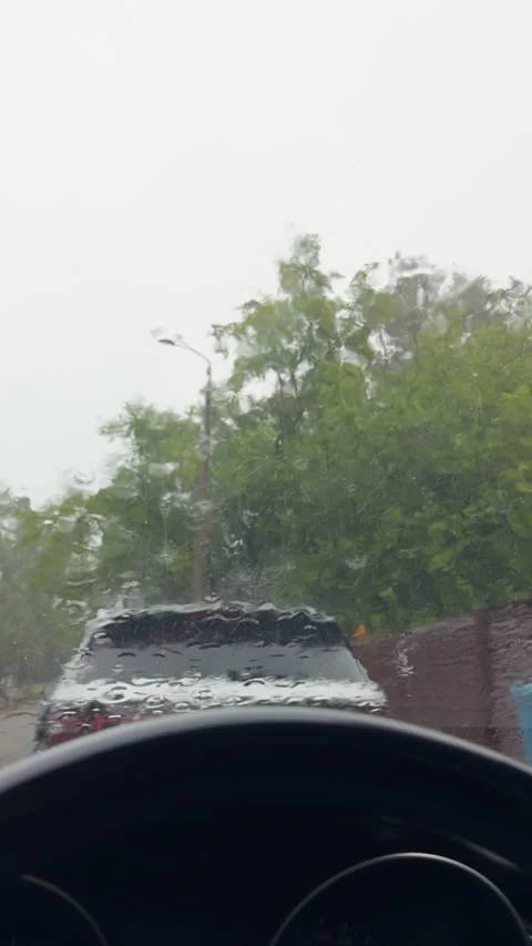 Rainy windshield view from car interior with blurred trees, streetlight, and Stockbeeldmateriaal 345530530