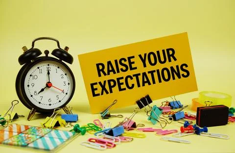 Raise Your Expectations text on paper card with stationery and alarm clock .. Stock Photos