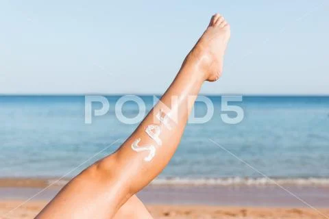 Raised up female leg with spf word made of sun cream at the beach. Sun protec Stock Photos