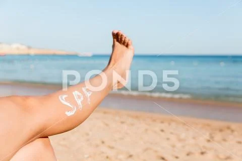 Raised up female leg with spf word made of sun cream at the beach. Sun protec Stock Photos