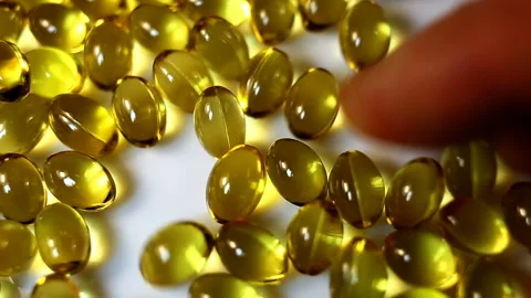 Rake small yellow capsules raining down on a white background. Real-time, close- Stock Footage 145107049