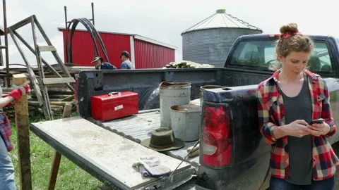 Ranchers using smart phone and unloading wooden fence posts from pickup truck Stock Footage 220360138