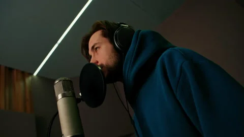 Rap singer with headphones and microphone emotionally recording new song in Stock Footage 237971200