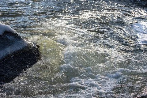 The rapid flow of the river breaks on a large stone covered with ice. The wat Stock Photos