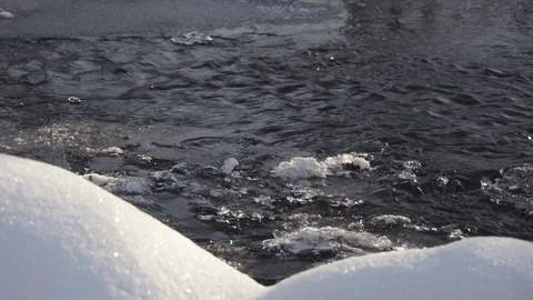 The rapid flow of the stream among the white snowdrifts of snow in the forest at Stock Footage 127006057