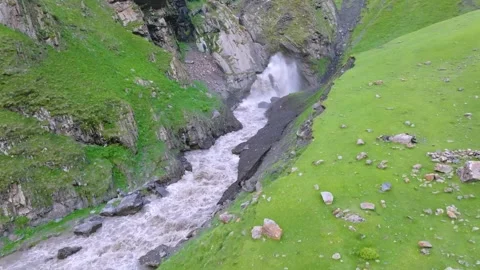 Rapid mountain river rushing over boulders in lush green gorge with a waterfall Stock Footage 325914305