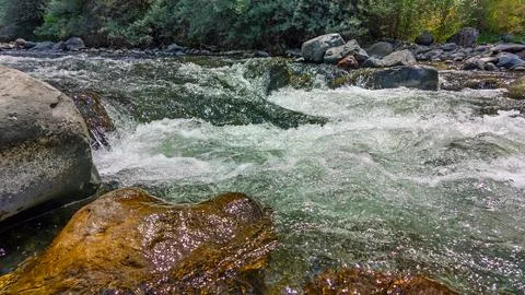 Rapid river current flows over large, weathered boulders Stock Photos