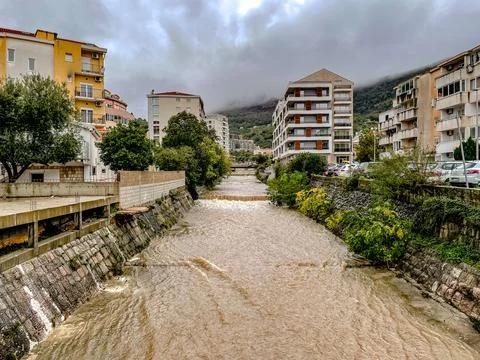 Rapid river flows past structures, poststorm river rushes past buildings with Stock Photos