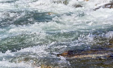 Rapid spring river flowing over rocks on sunny day, forming white water waves Stock Photos