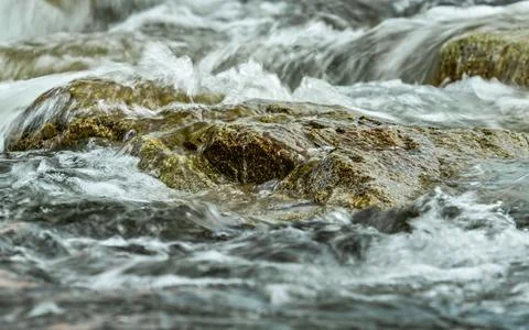 Rapid spring river flowing over rocks forming white water waves, closeup de.. Stock Photos