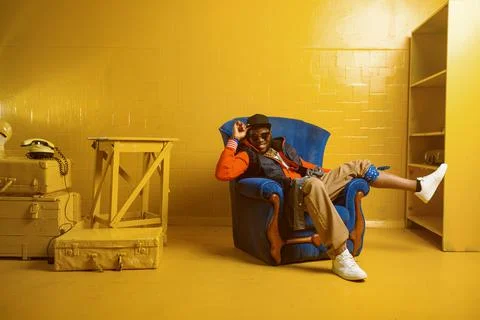 Rapper posing in chair in studio with yellow tones Stock Photos