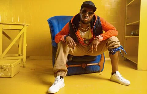 Rapper posing in chair in studio with yellow tones Foto stock